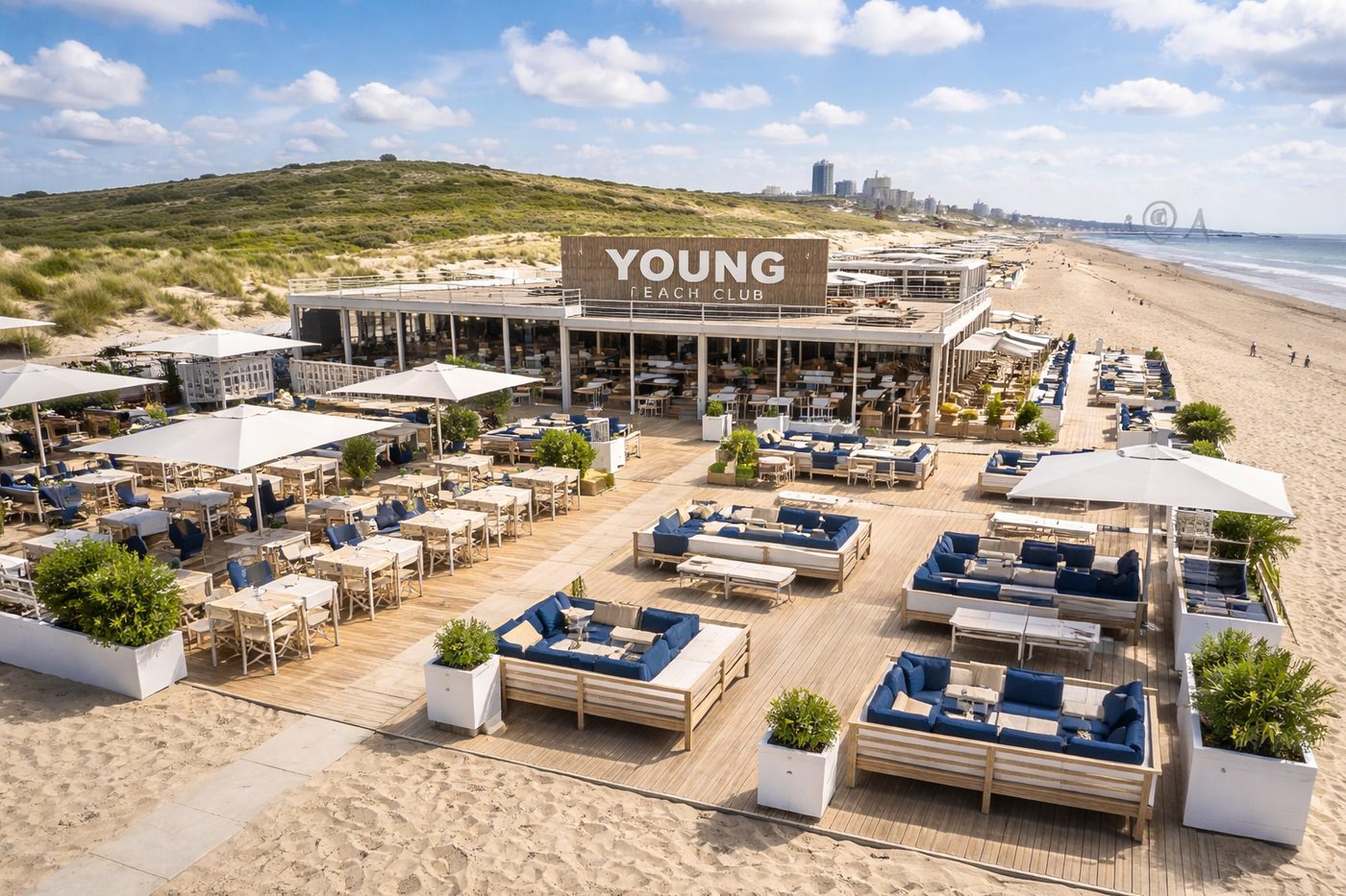 An aerial view of YOUNG Beach Club, its name written across the roof, with the Scheveningen skyline behind