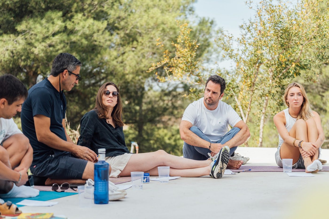 Members sitting in a circle on mats under the trees