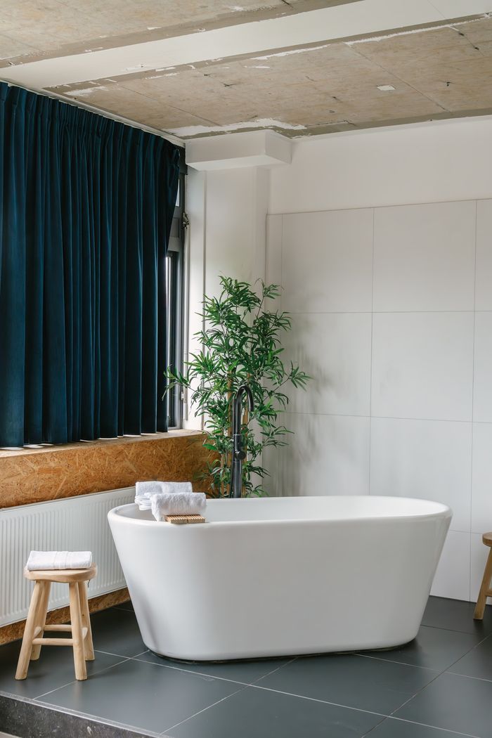 A freestanding bath under a raw concrete ceiling in a YOUNG hotel room