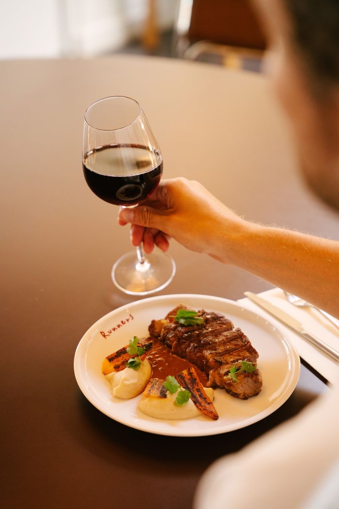 A guest raising a glass of red wine over a plate at Runners